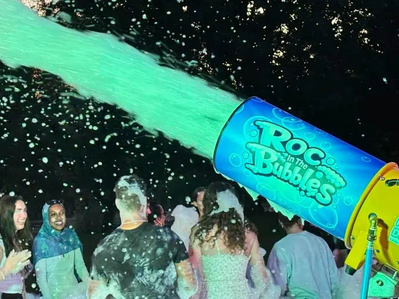 A ROC in the Bubbles cannon sending a glowing green stream of foam over a crowd of young adults at night.